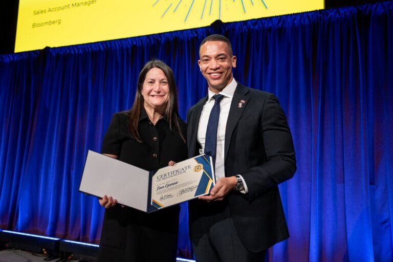 Nancy Cutler and Ian Genao stand on stage, holding a certificate.