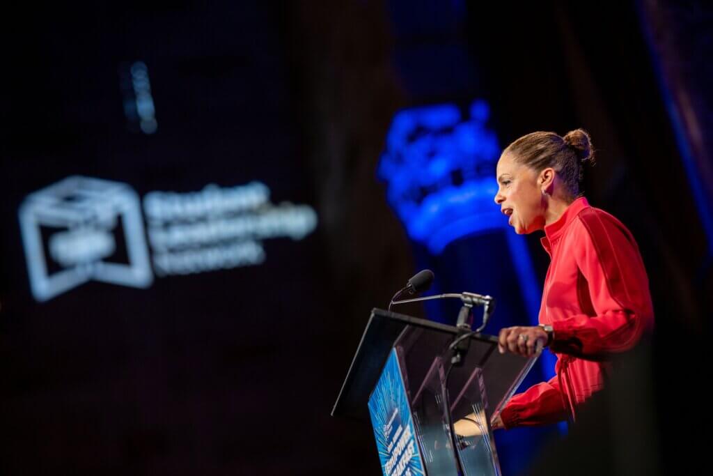 Soledad O'Brien speaks at a podium on stage, with the words Student Leadership projected on the wall behind her.