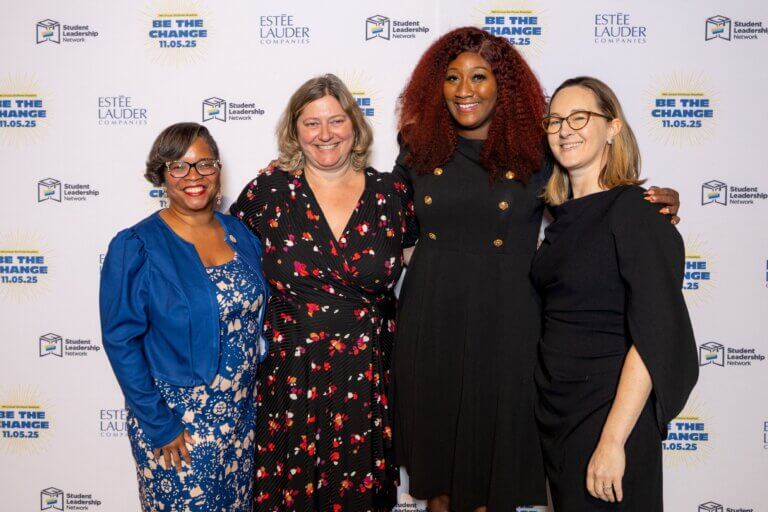 Four women school principals stand together and smile in front of a step-and-repeat banner