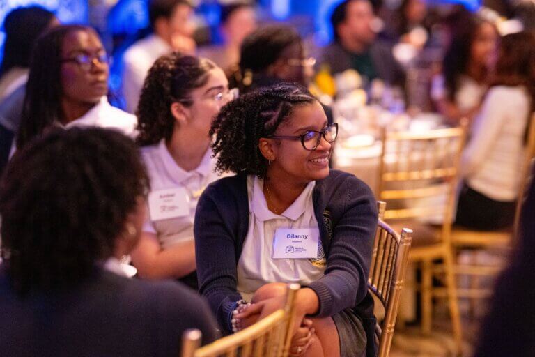 A student listens attentively, seated at a formal event table
