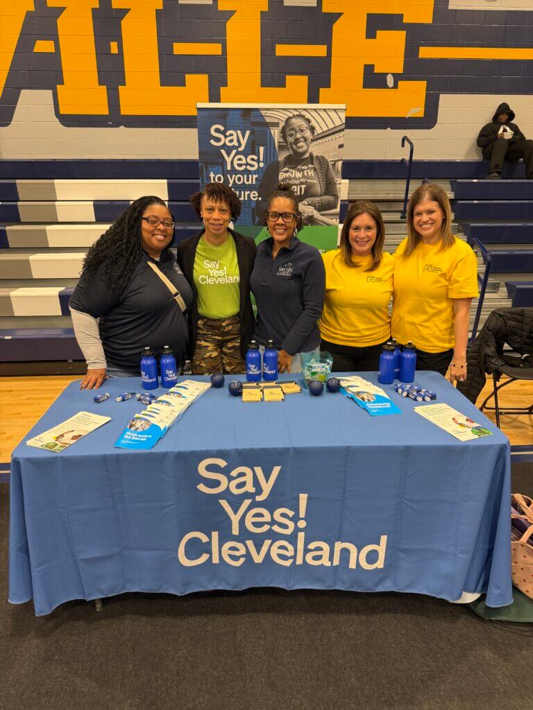 Five women stand behind a table covered with a Say Yes! Cleveland tablecloth and informational materials at HBCU college fair visit