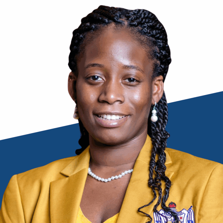 A woman with braided hair wearing a yellow blazer, pearl necklace, and earrings poses in front of a white and blue background.