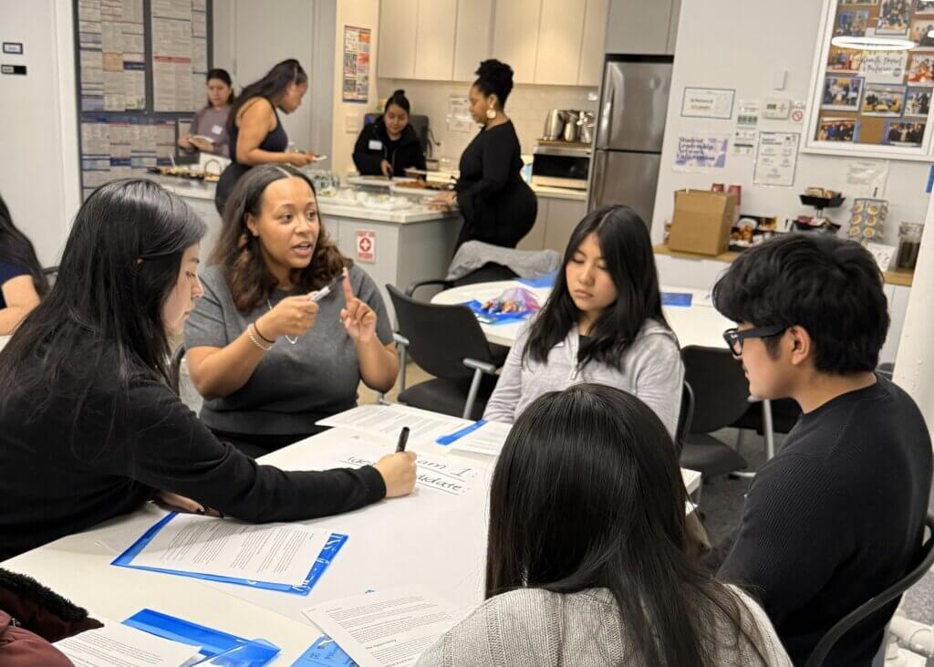 A woman speaks to three students seated at a table with internship worksheets in front of them