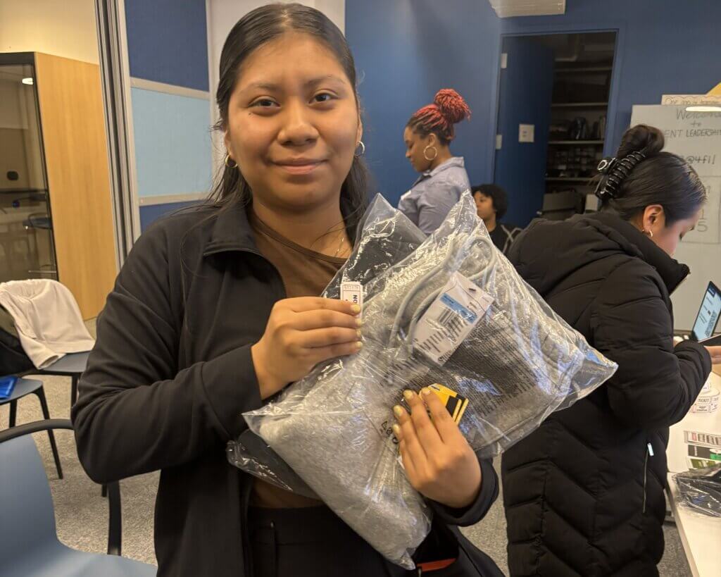 A student raffle prize winner holds up Nike Jordan clothing and Metrocards from the prize table