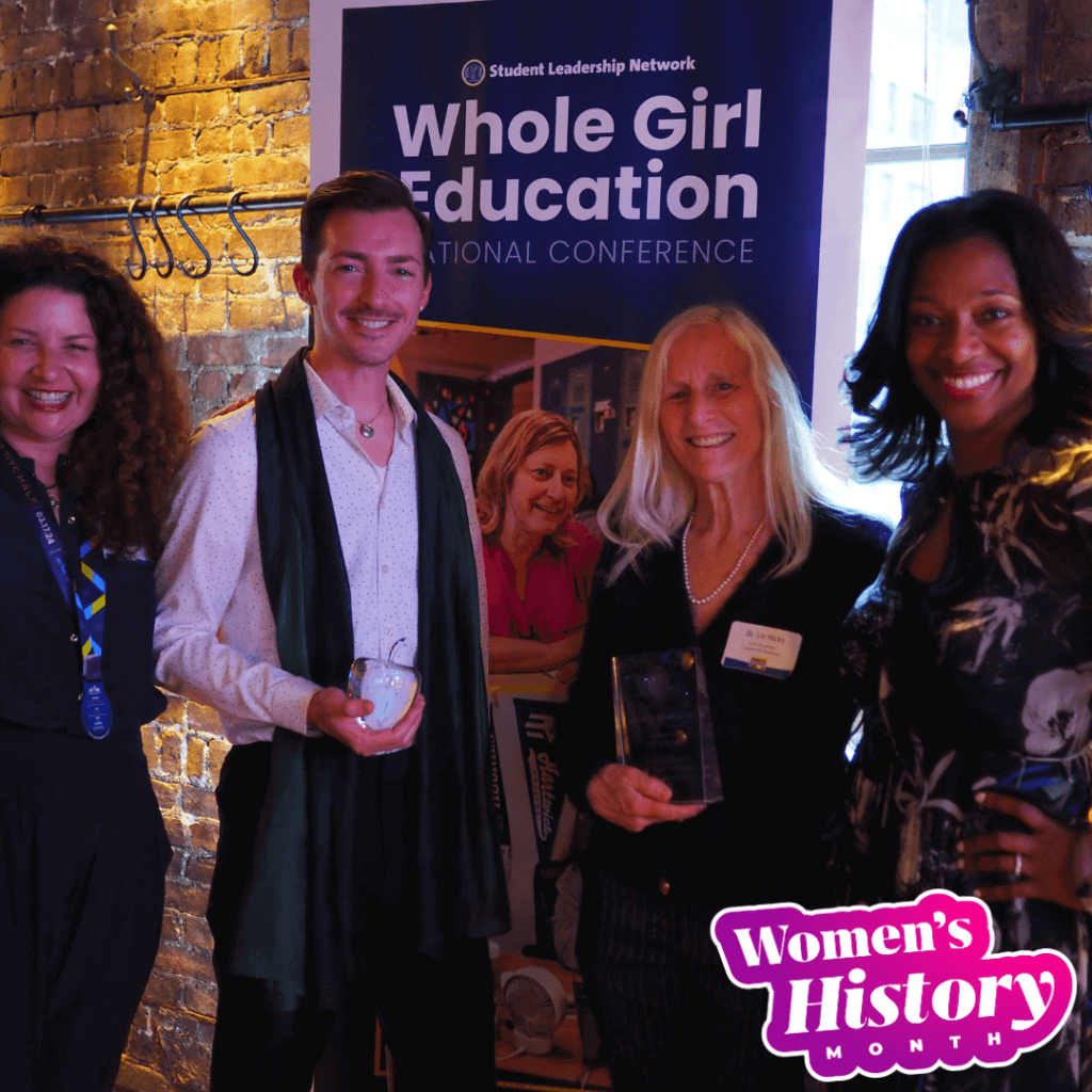 Four people stand smiling in front of a Whole Girl Education conference banner, holding awards that celebrate leadership. A Women's History Month graphic is in the bottom right corner.