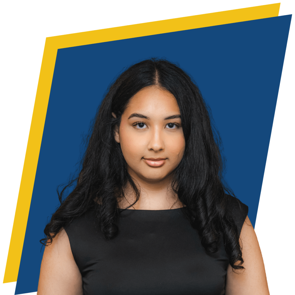 A young woman with long black hair wearing a black sleeveless top stands in front of a blue and yellow-bordered frame for a first-gen student story headshot.