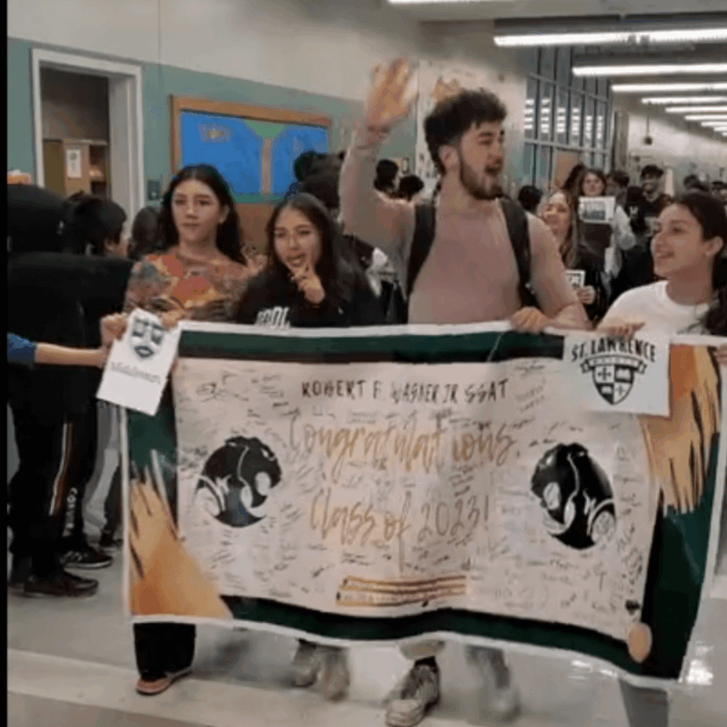 A group of students walk down a school hallway holding a large banner that reads Congratulations Class of 2023, showcasing their leadership as they display signatures and two school logos with pride.