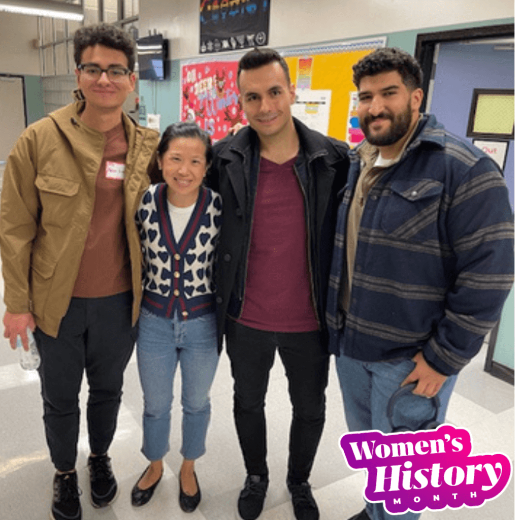 Four people stand together in a hallway, smiling at the camera and celebrating leadership. A Womens History Month graphic is in the bottom right corner.