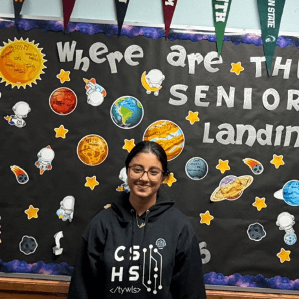 A student stands in front of a bulletin board at TYWLS Astoria, decorated with space-themed cutouts and the words Where are the seniors landing?, highlighting a student spotlight among producing stars.