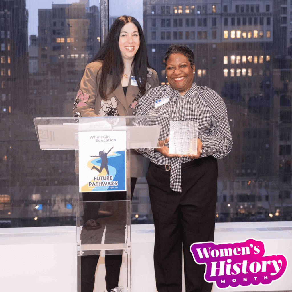 Two women stand together at a podium with a city view behind them; one holds an award, highlighting their leadership. A Women’s History Month graphic is in the lower right corner.