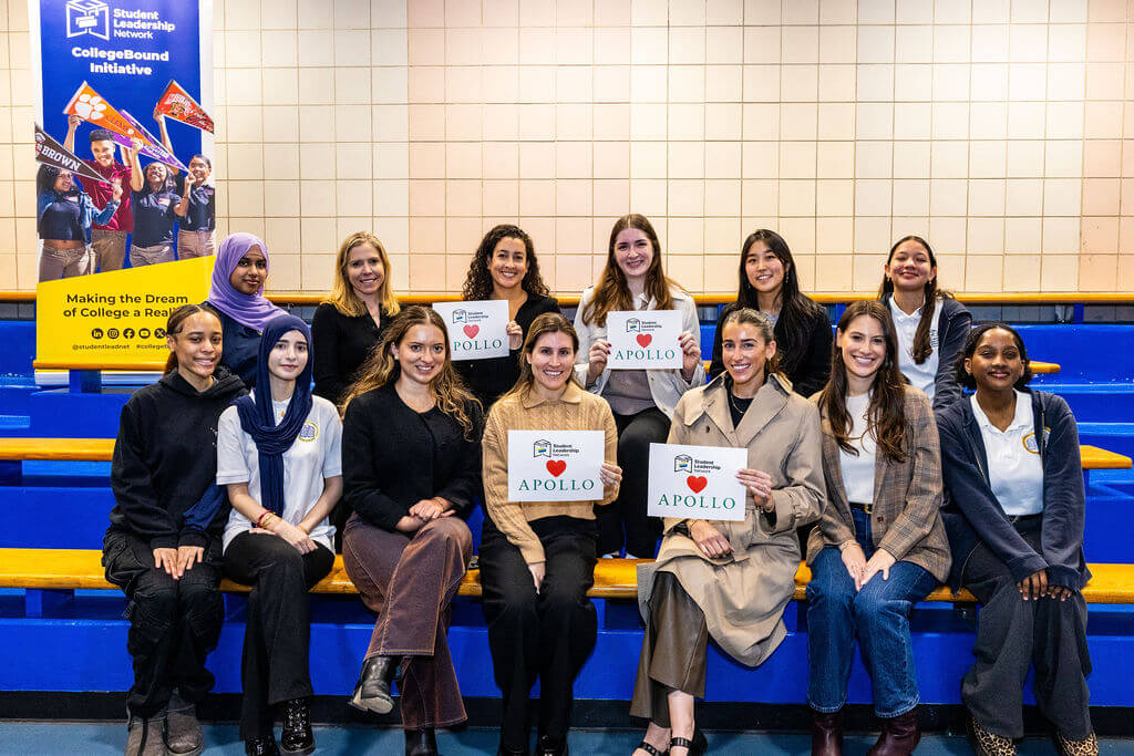 A group of thirteen people poses indoors in front of bleachers; three hold signs that read Student Leadership Network, CollegeBound Initiative, Apollo.