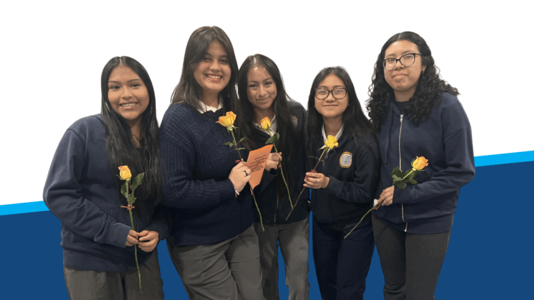 Five young women in uniforms stand together holding yellow roses and a card, smiling at the camera against a white and blue background.