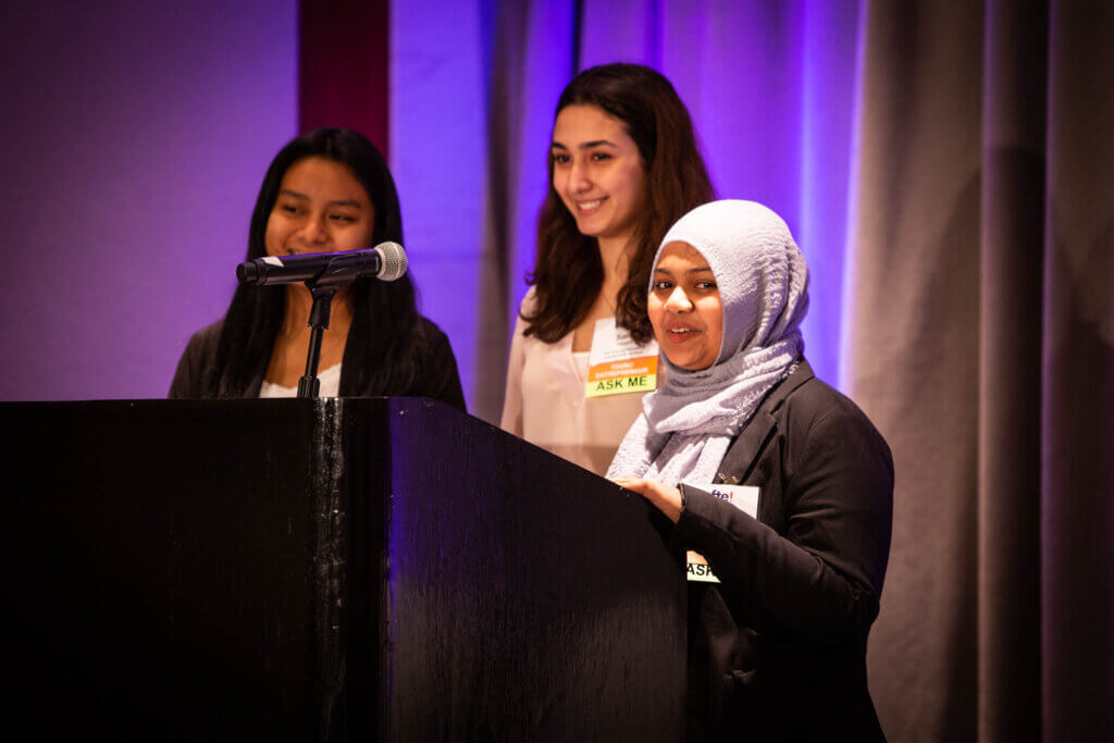 Three students stand at a podium with microphones