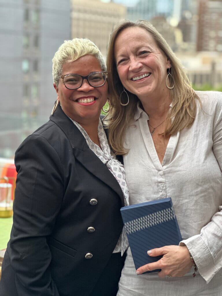 Two women standing side by side outdoors, smiling at the camera for the network's April Blount Awards