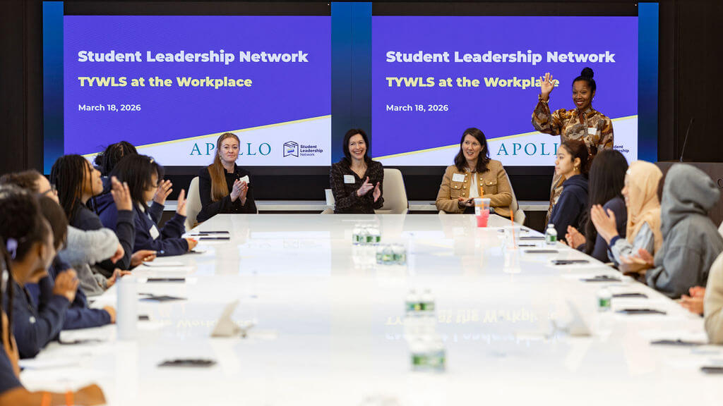 A group of people sit around a conference table while four women speak at the front; two screens display Apollo Opportunity Foundation and Student Leadership Network TYWLS at the Workplace, March 18, 2026.