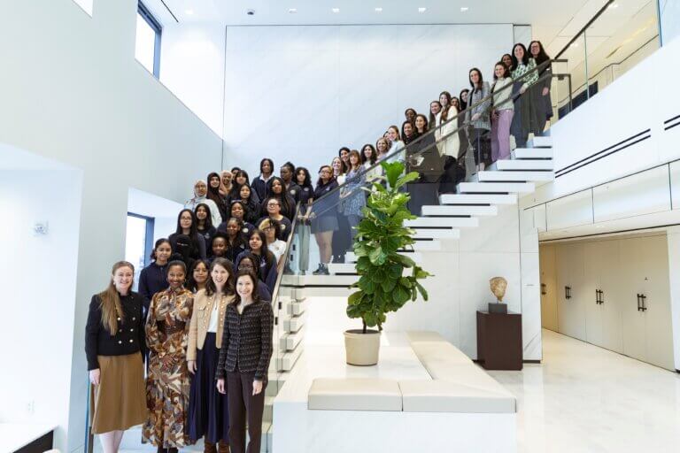 A large group of women, gathered for an Apollo Opportunity Foundation event, posed together on and around a modern white staircase inside a spacious, well-lit building