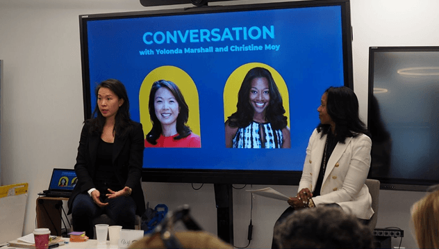 Two women sit and talk in front of a screen displaying the text CONVERSATION with Yolonda Marshall and Christine Moy