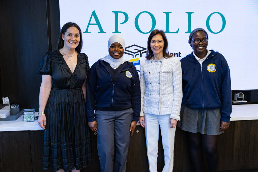 Four women stand side by side, smiling, in front of a screen displaying the word APOLLO and a logo. Two wear hijabs and school uniforms; two wear business attire—gathered for the 2025 Annual Report presentation.