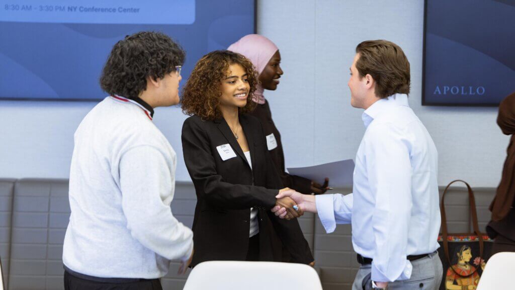 Three people in business attire greet each other with a handshake, representing an Apollo Opportunity Foundation meeting