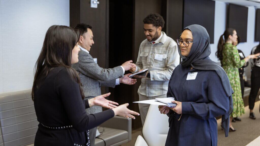 Several people stand in pairs, conversing and holding papers in a modern conference room during an Apollo Opportunity Foundation event.