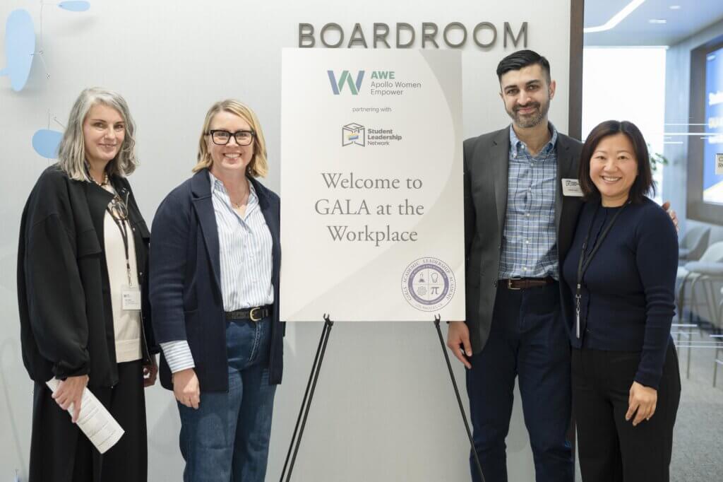 Four people stand beside a sign that reads Welcome to GALA at the Workplace in a conference room setting