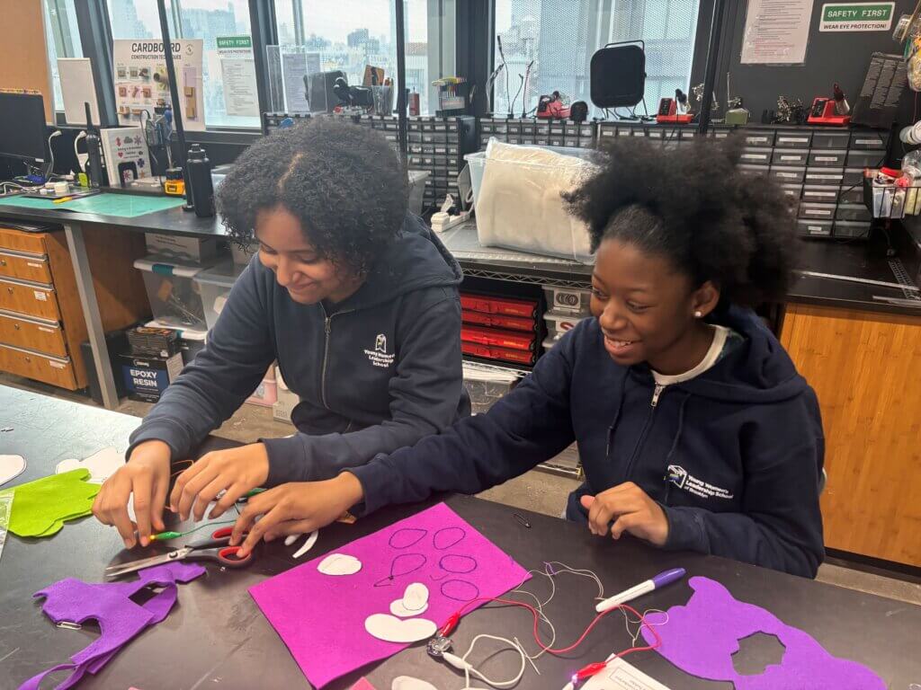 Two students collaborate on a craft project using felt, scissors, and wires at a table