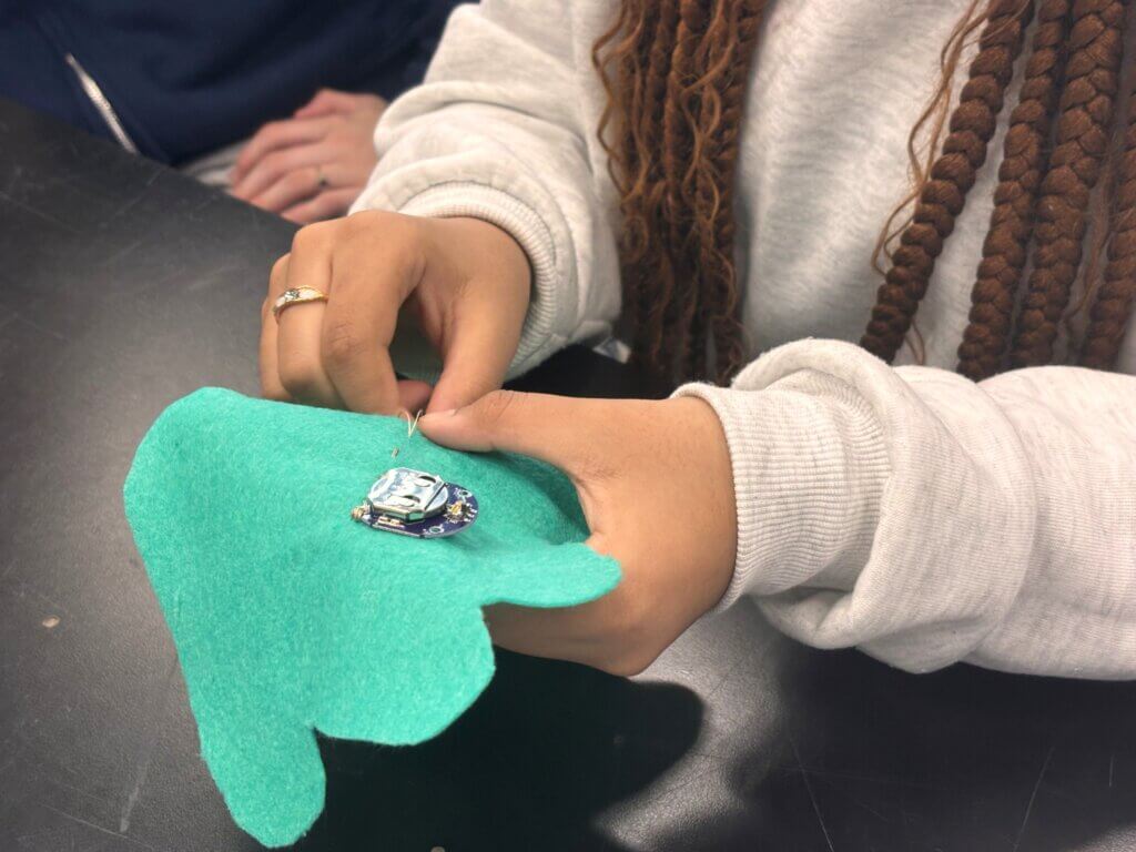 Person sewing an electronic component onto a piece of green felt as part of a STEM exposure activity