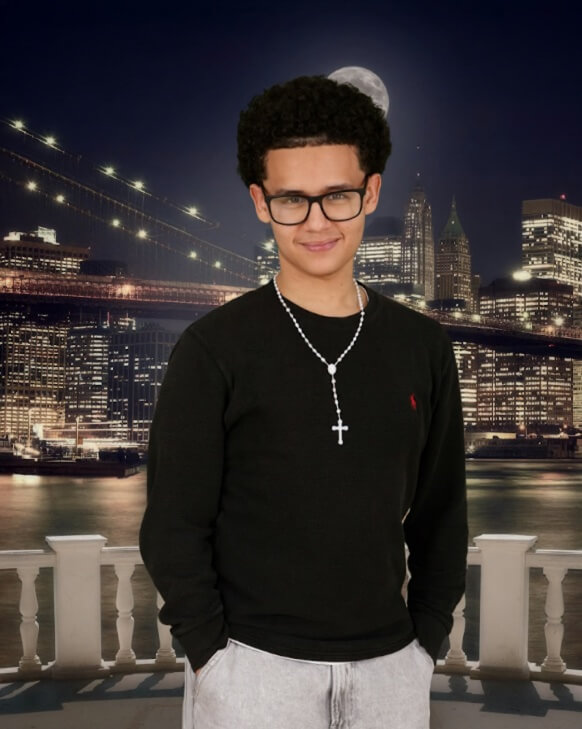 A young person wearing glasses, a black shirt, and a cross necklace stands in front of a nighttime city skyline and bridge, reminiscent of the iconic views associated with Jeffrey Gural’s urban developments.