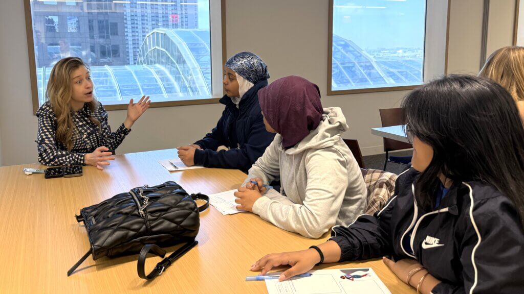 A woman gestures while speaking to students about career exposure in an office setting