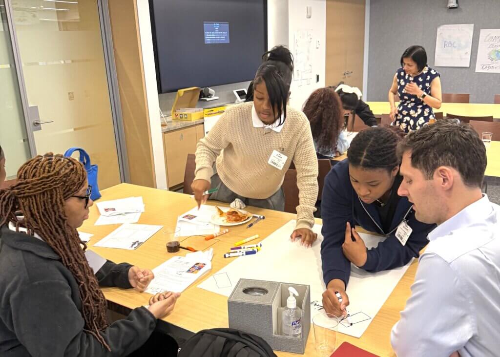 Four people collaborate on a project at a table with markers and paper, during career exploration activity