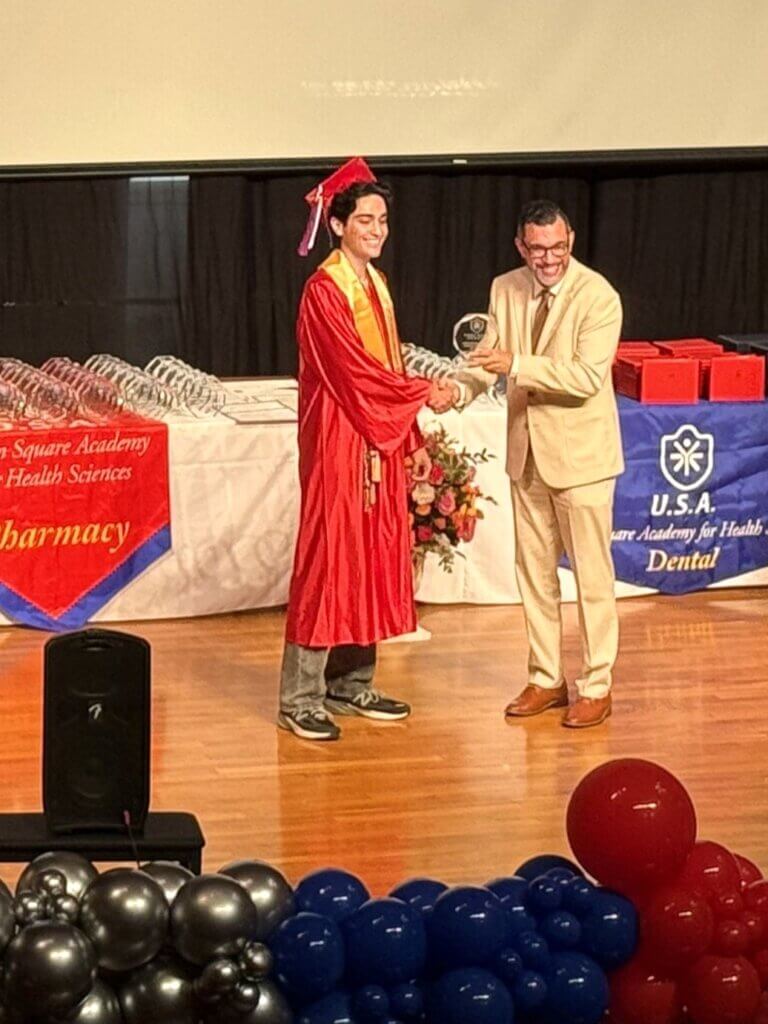 A student in a red graduation gown receives an award from the principal on stage