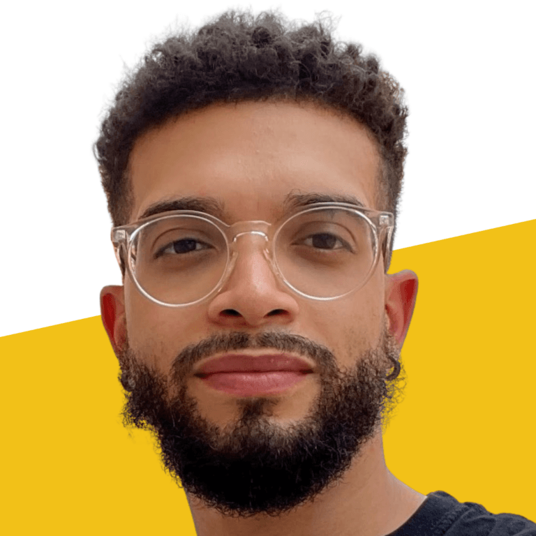 Carlos Grimes, a man with curly hair, glasses, and a beard, wearing a black shirt, poses in front of a white and yellow background.