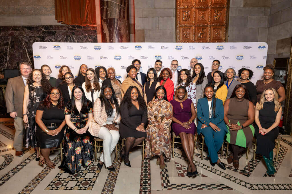 A large group of professionally dressed people pose for a photo in an ornate room with a patterned floor and a step-and-repeat backdrop, capturing the moment at the 2025 Annual Report event.