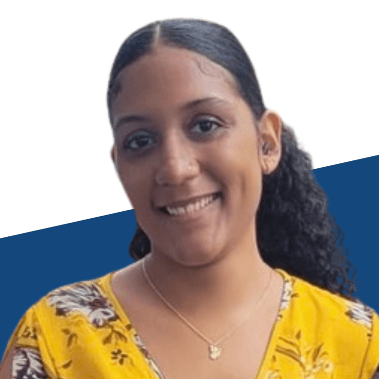A woman with long curly hair, wearing a yellow floral top and a necklace, smiles at the camera against a blue and white background—capturing the radiant presence of Shaira Polanco.