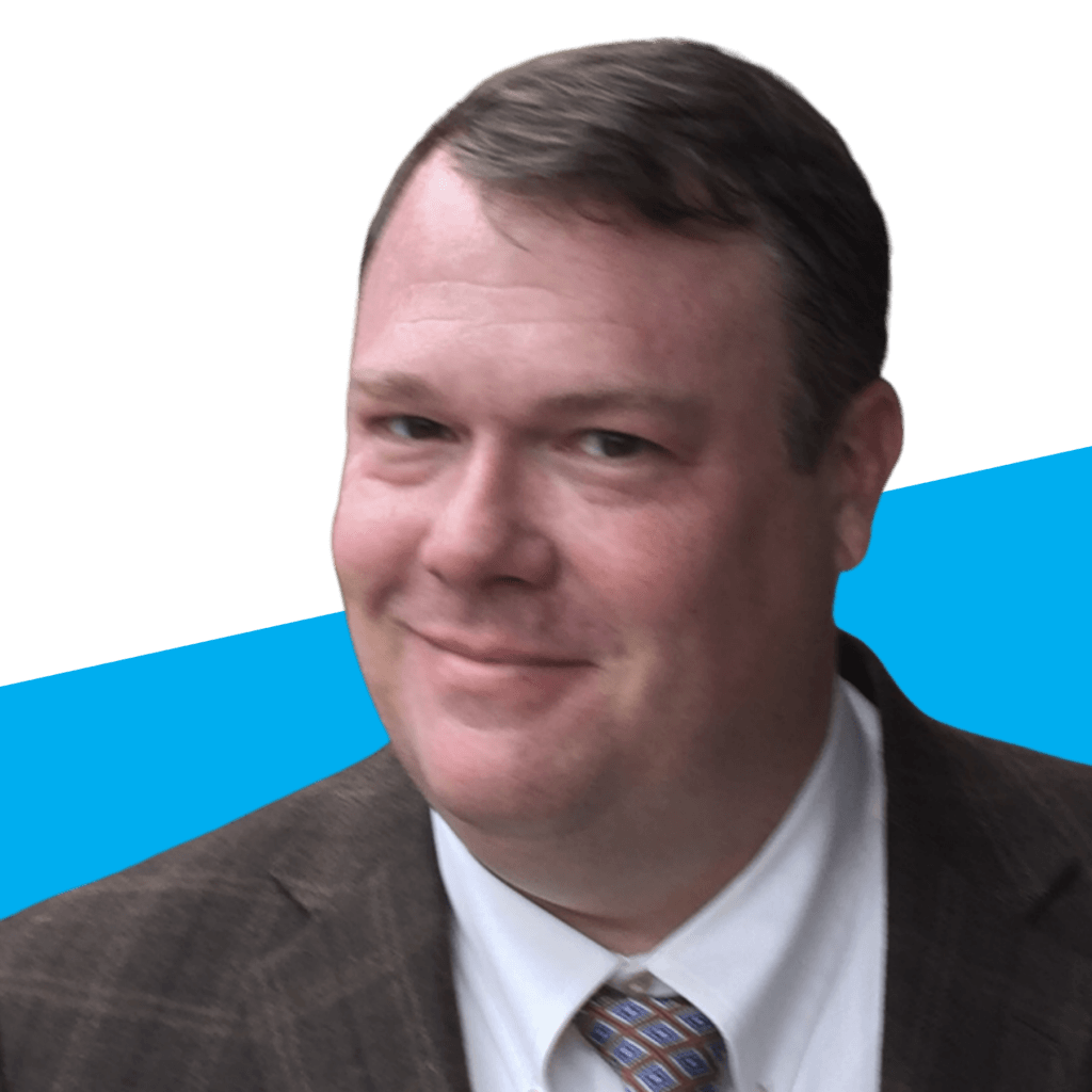 Man in a brown plaid suit jacket and patterned tie smiles at the camera against a white and blue background, embodying the spirit of Voices Behind the Mission.