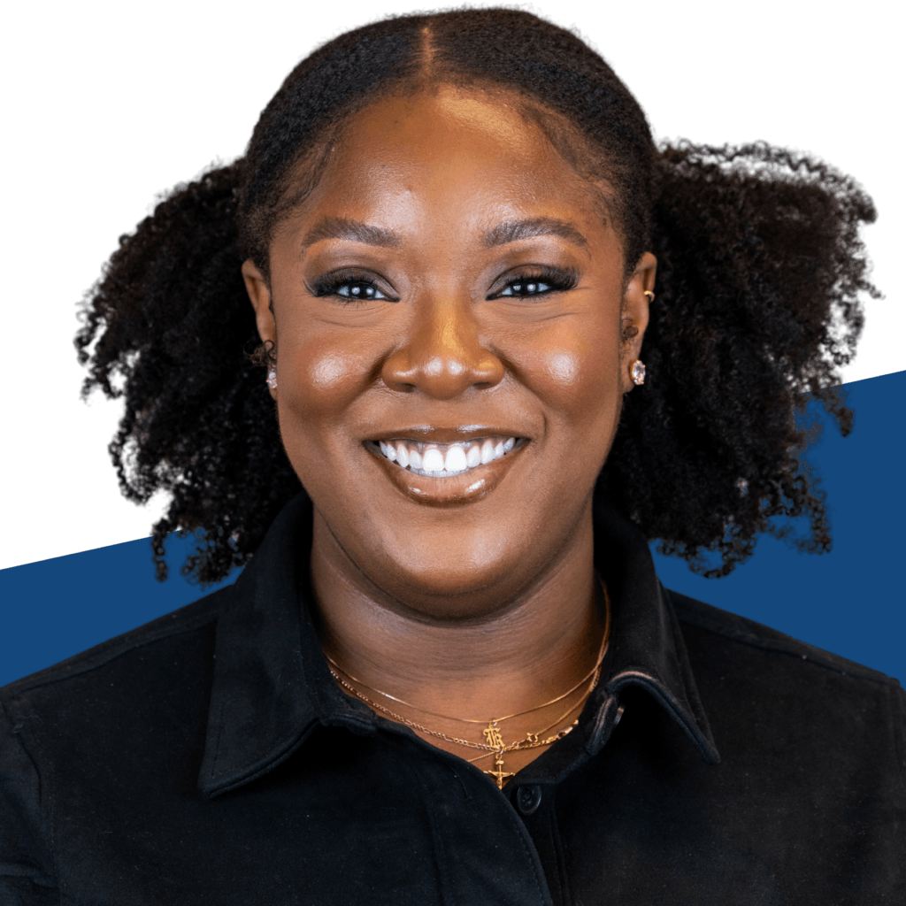 A woman with curly black hair smiles at the camera, embodying the spirit of “Voices Behind the Mission,” as she wears a black collared shirt and layered gold necklaces, against a white and blue background.