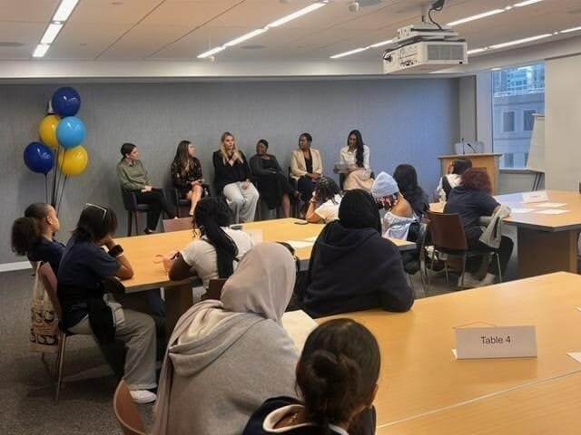 A panel of six women, including Angela Nimoh from RBC Capital Markets, speaks to an audience seated at tables in a conference room adorned with balloons and a window in the background, discussing topics related to securitization finance.