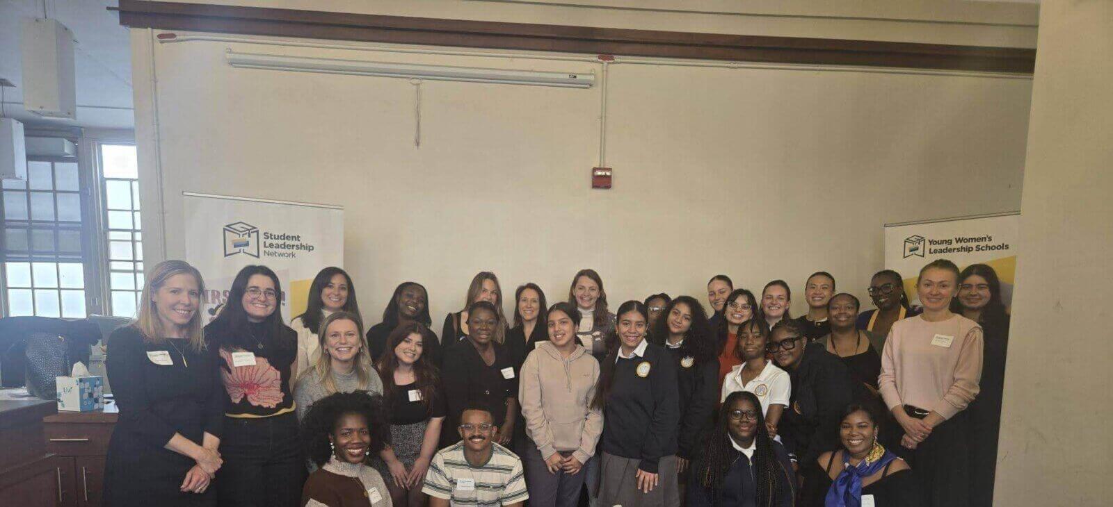 Group photo of diverse women and students standing and sitting indoors, posing in front of Student Leadership Network and Young Womens Leadership Schools banners, including Angela Nimoh from RBC Capital Markets’ Securitization Finance team.