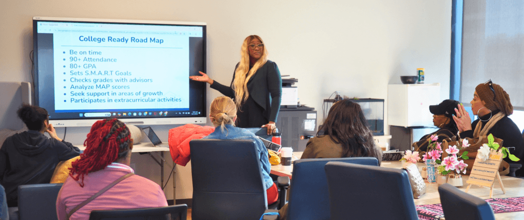 A WholeGirl+ school leader stands at the front of a classroom gesturing to a digital screen titled College Ready Road Map