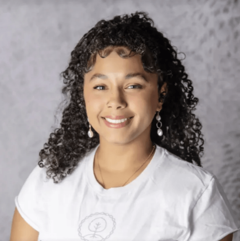 Portrait of a smiling Kansas City Girls Prep assistant principal with curly hair, wearing a white t-shirt and drop earrings.