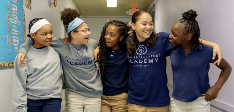 Five students from Girls Preparatory Academy Kansas City with their arms around each other’s shoulders in a school hallway.