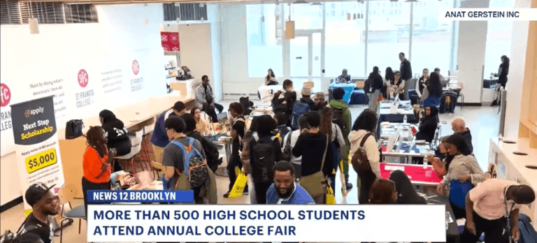 A large group of high school students and college admissions rep gather at tables during a college fair in a bright indoor space.